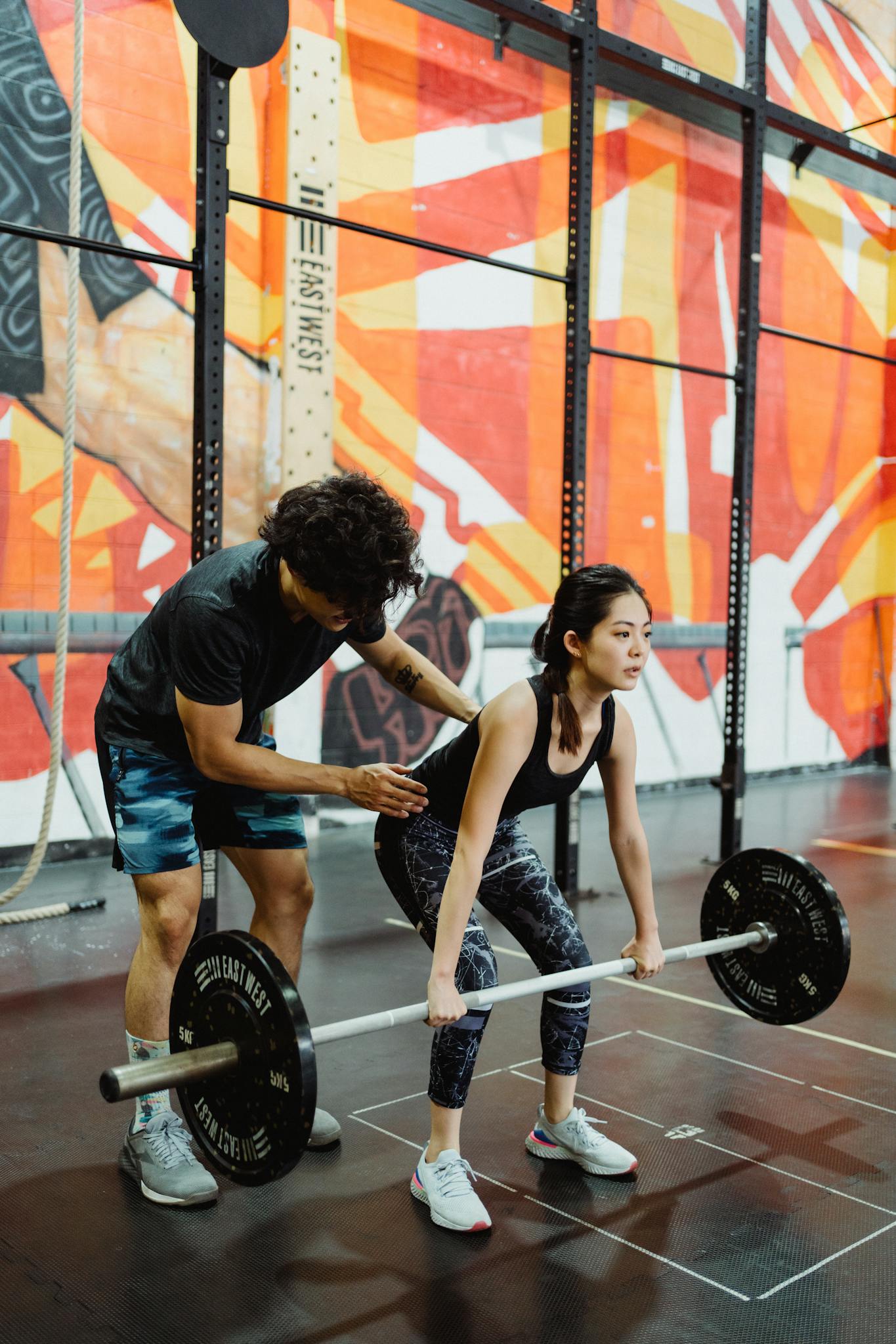 A young woman lifting a barbell in a gym with a trainer's guidance. Perfect for fitness and training themes.